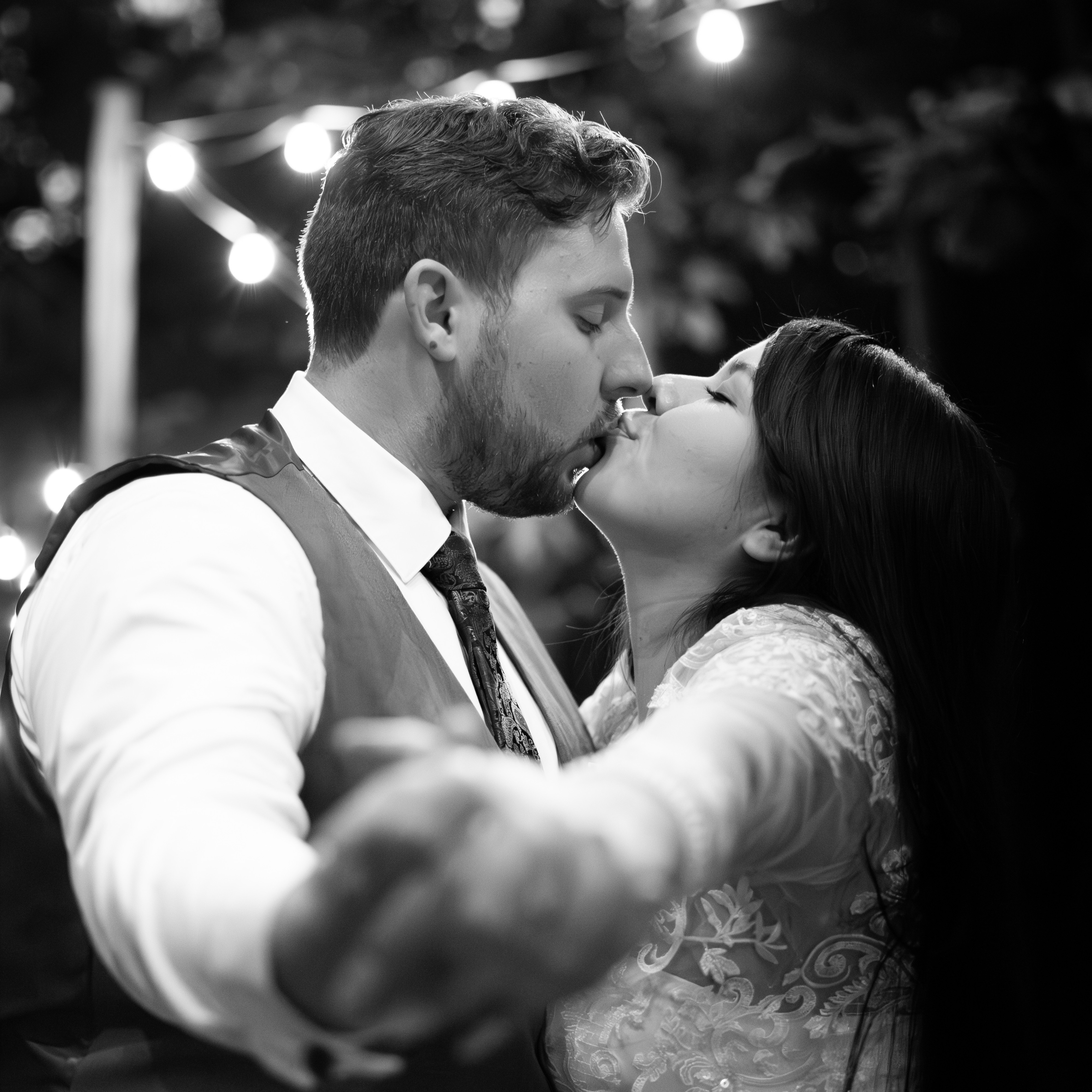 Black-and-white photograph of a couple kissing under string lights