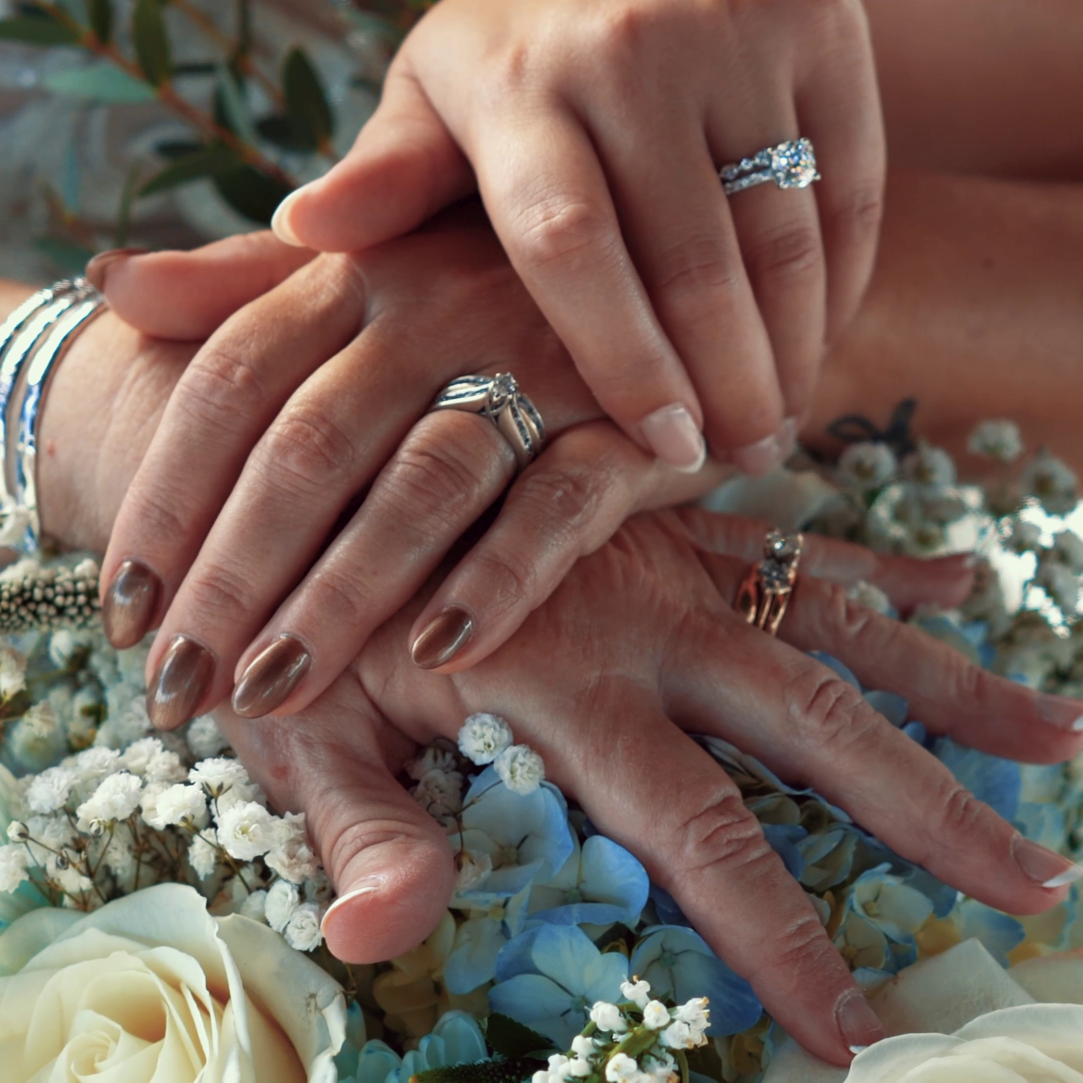 Close-up of wedding rings on the stacked hands of a couple over a floral bouquet